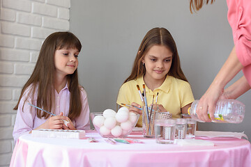 Image showing Mom pours vinegar into glasses with food coloring, children at the table prepare to paint eggs