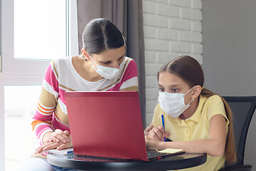 Image showing The tutor at home in a medical mask explains to the girl the course of solving homework