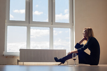 Image showing Upset girl in an empty room sitting on the floor with a glass of wine