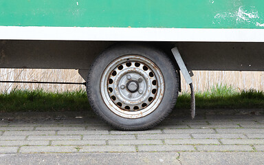 Image showing Wheel of an old green wooden trailer on wheels stands at the sid