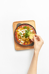 Image showing Woman\'s hand takes Shakshouka healthy food from the pan.