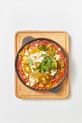 Image showing Shakshuka dish with pita bread in a pan on a wooden board.