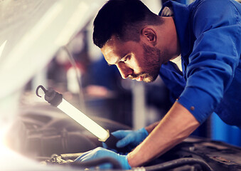 Image showing mechanic man with lamp repairing car at workshop