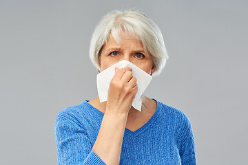 Image showing sick senior woman blowing nose to paper napkin