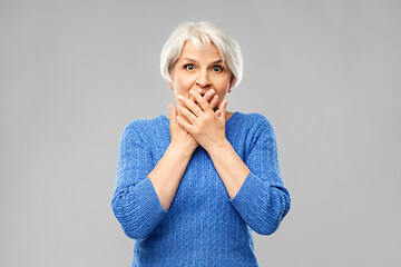 Image showing confused senior woman covering her mouth by hands