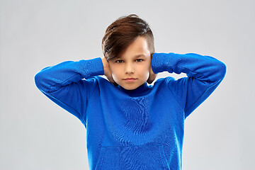 Image showing stressed boy in blue sweater closing ears by hands