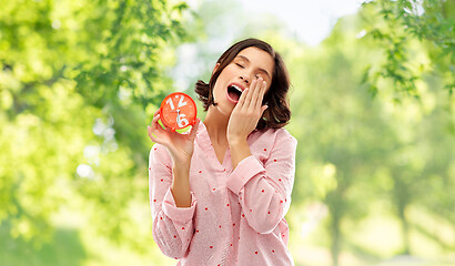 Image showing sleepy woman in pajama with alarm clock yawning