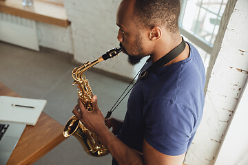 Image showing African-american musician playing saxophone during online concert at home isolated and quarantined, impressive improvising