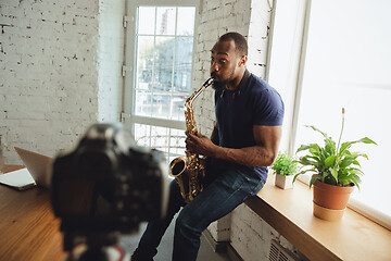 Image showing African-american musician playing saxophone during online concert at home isolated and quarantined, impressive improvising