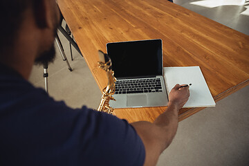 Image showing African-american musician playing saxophone during online concert at home isolated and quarantined. Blank laptop screen with copyspace.