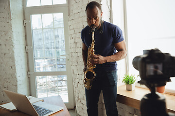 Image showing African-american musician playing saxophone during online concert at home isolated and quarantined, improvising on camera