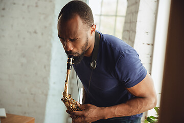 Image showing African-american musician playing saxophone during online concert at home isolated and quarantined, attented, focused