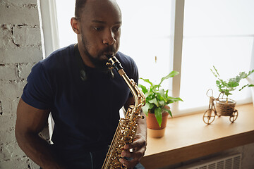 Image showing African-american musician playing saxophone during online concert at home isolated and quarantined, impressive improvising