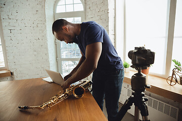 Image showing African-american musician playing saxophone during online concert at home isolated and quarantined, attented, focused