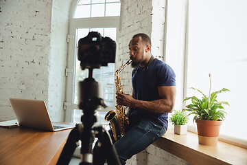 Image showing African-american musician playing saxophone during online concert at home isolated and quarantined