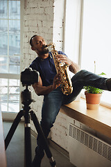 Image showing African-american musician playing saxophone during online concert at home isolated and quarantined, impressive improvising