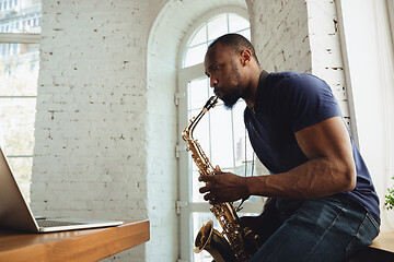 Image showing African-american musician playing saxophone during online concert at home isolated and quarantined, impressive improvising