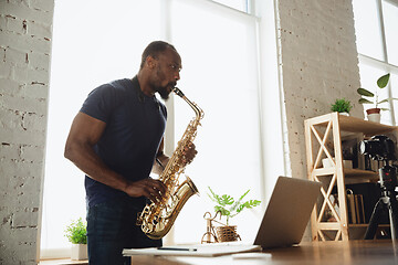 Image showing African-american musician playing saxophone during online concert at home isolated and quarantined