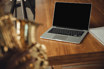 Image showing African-american musician playing saxophone during online concert at home isolated and quarantined. Blank laptop screen with copyspace.