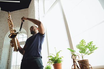 Image showing African-american musician playing saxophone during online concert at home isolated and quarantined, attented, focused