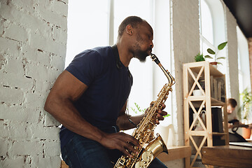 Image showing African-american musician playing saxophone during online concert at home isolated and quarantined, impressive improvising