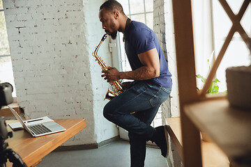 Image showing African-american musician playing saxophone during online concert at home isolated and quarantined, impressive improvising