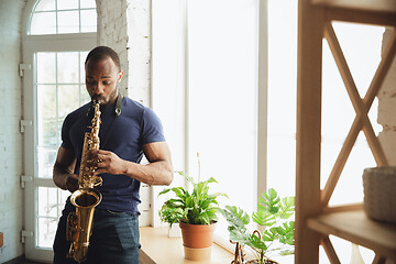 Image showing African-american musician playing saxophone during online concert at home isolated and quarantined, attented, focused