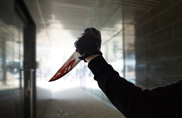 Image showing hand in glove with blood on knife over dark tunnel