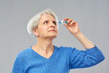 Image showing senior woman with dry eye syndrome using drops