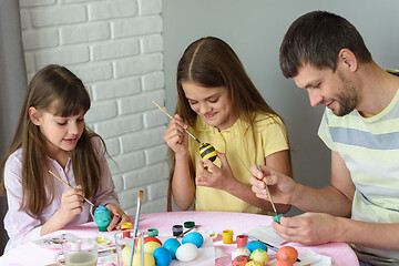 Image showing Dad with two daughters paint eggs for Easter holiday