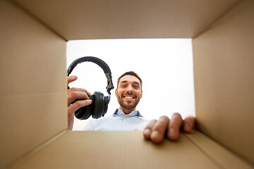 Image showing smiling man taking headphones out of parcel box