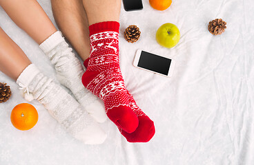 Image showing Soft photo of woman and man on the bed with phone and fruits, top view point. Female and male legs in warm woolen socks