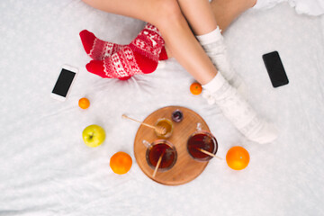 Image showing Soft photo of woman and man on the bed with phone and fruits, top view point. Female and male legs in warm woolen socks