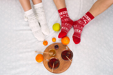 Image showing Soft photo of woman and man on the bed with tea and fruits, top view point. Female and male legs in warm woolen socks