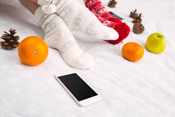 Image showing Soft photo of woman and man on the bed with phone and fruits, top view point. Female and male legs in warm woolen socks