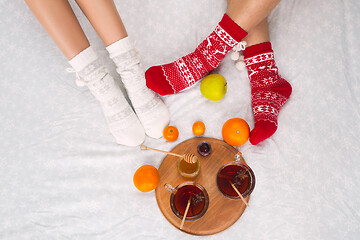 Image showing Soft photo of woman and man on the bed with tea and fruits, top view point. Female and male legs in warm woolen socks