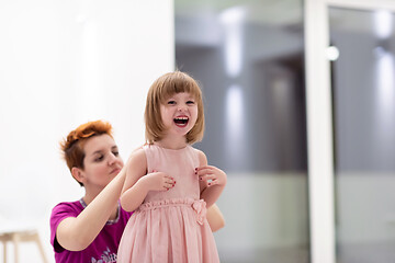 Image showing young mother helping daughter while putting on a dress