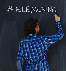 Image showing Teen Boy with chalk  writing on black chalkboard hashtag elearni