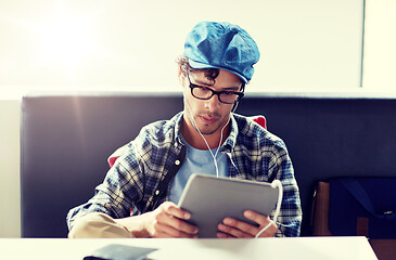 Image showing man with tablet pc and earphones sitting at cafe