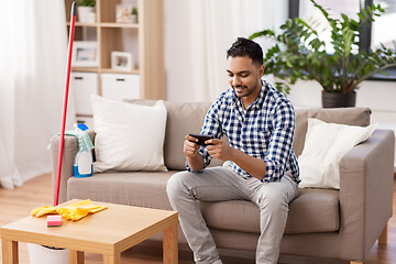 Image showing man playing game on smartphone after cleaning home