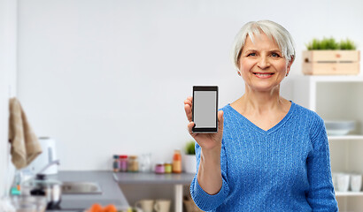 Image showing smiling senior woman showing smartphone in kitchen