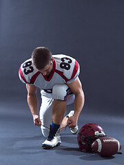 Image showing American Football Player tie his shoe laces isolated on gray