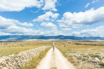 Image showing Caucasian young woman in summer dress holding bouquet of lavender flowers while walking outdoor through dry rocky Mediterranean Croatian coast lanscape on Pag island in summertime