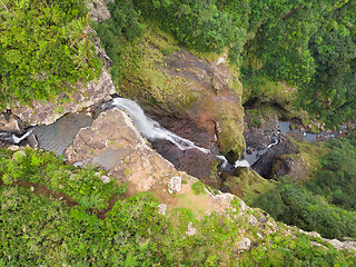 Image showing Aerial top view of travel couple waving to drone, standing on the edge of 500 feet waterfall in the tropical island jungle of Black river gorges national park on Mauritius island