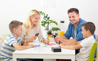 Image showing Happy young family playing card game at dining table at bright modern home.