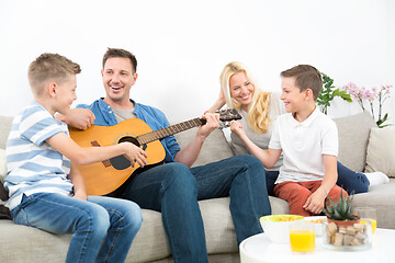 Image showing Happy caucasian family smiling, playing guitar and singing songs together at cosy modern home