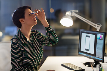 Image showing female designer using eye drops at night office