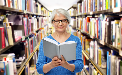 Image showing senior woman in glasses reading book at library