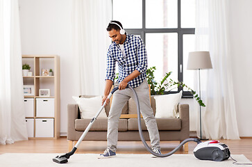 Image showing man in headphones with vacuum cleaner at home