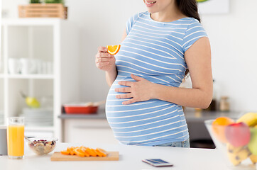 Image showing close up of pregnant woman eating orange at home